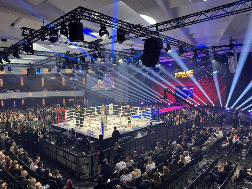 Blick auf den vollen Veranstaltungsraum und Boxring beim Fame Fighting 2024 in Bonn. Die Bühne ist mit intensiver Beleuchtung und modernen Lichteffekten ausgestattet, während Zuschauer gespannt die Kämpfe verfolgen.